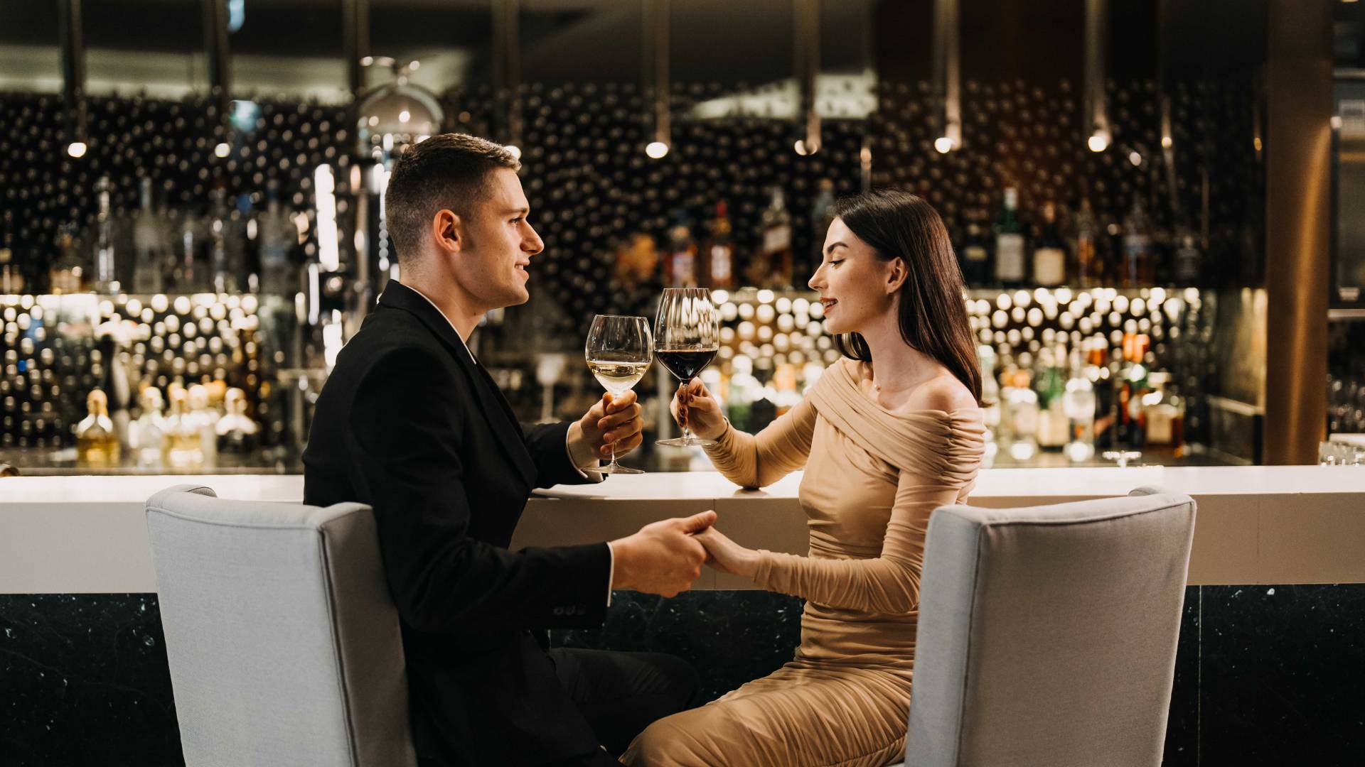 Couple holding hands at the bar and holding wine glasses