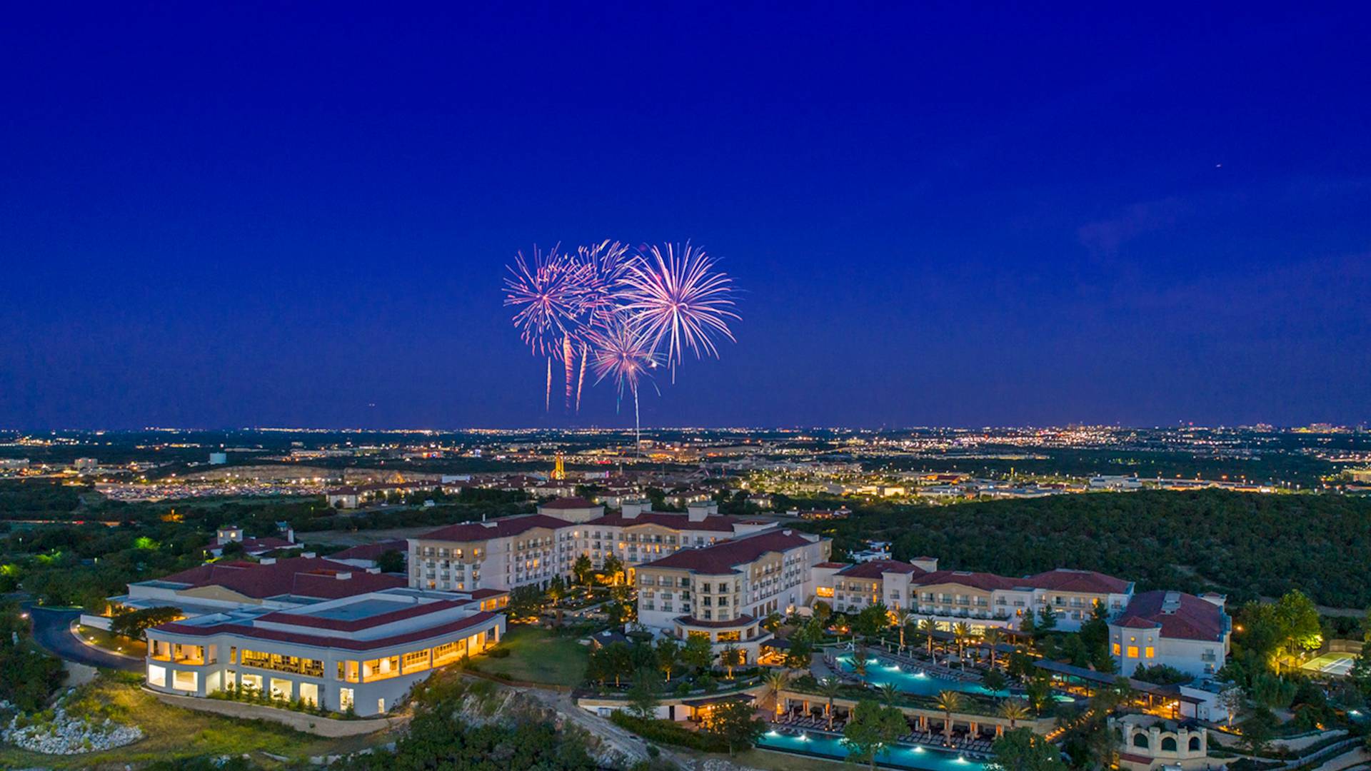Aerial view of hotel and grounds at night with fireworks in the sky-transition