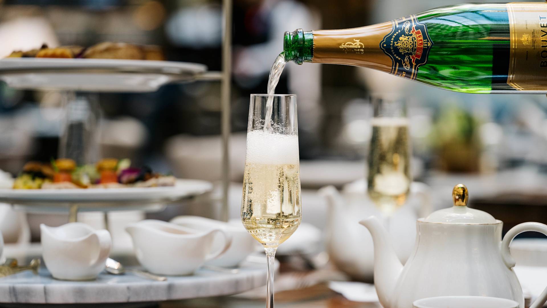 Champán que se vierte en una copa con el té de la media tarde en la transición de fondo