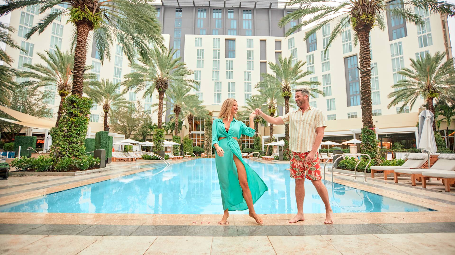 Pria dan wanita berjalan di tepi kolam renang dengan tangan digenggam bersama