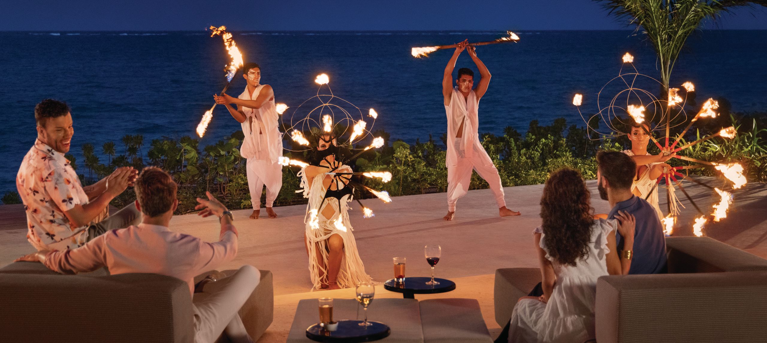 Guests watch and cheer for fire dancers in front of the ocean