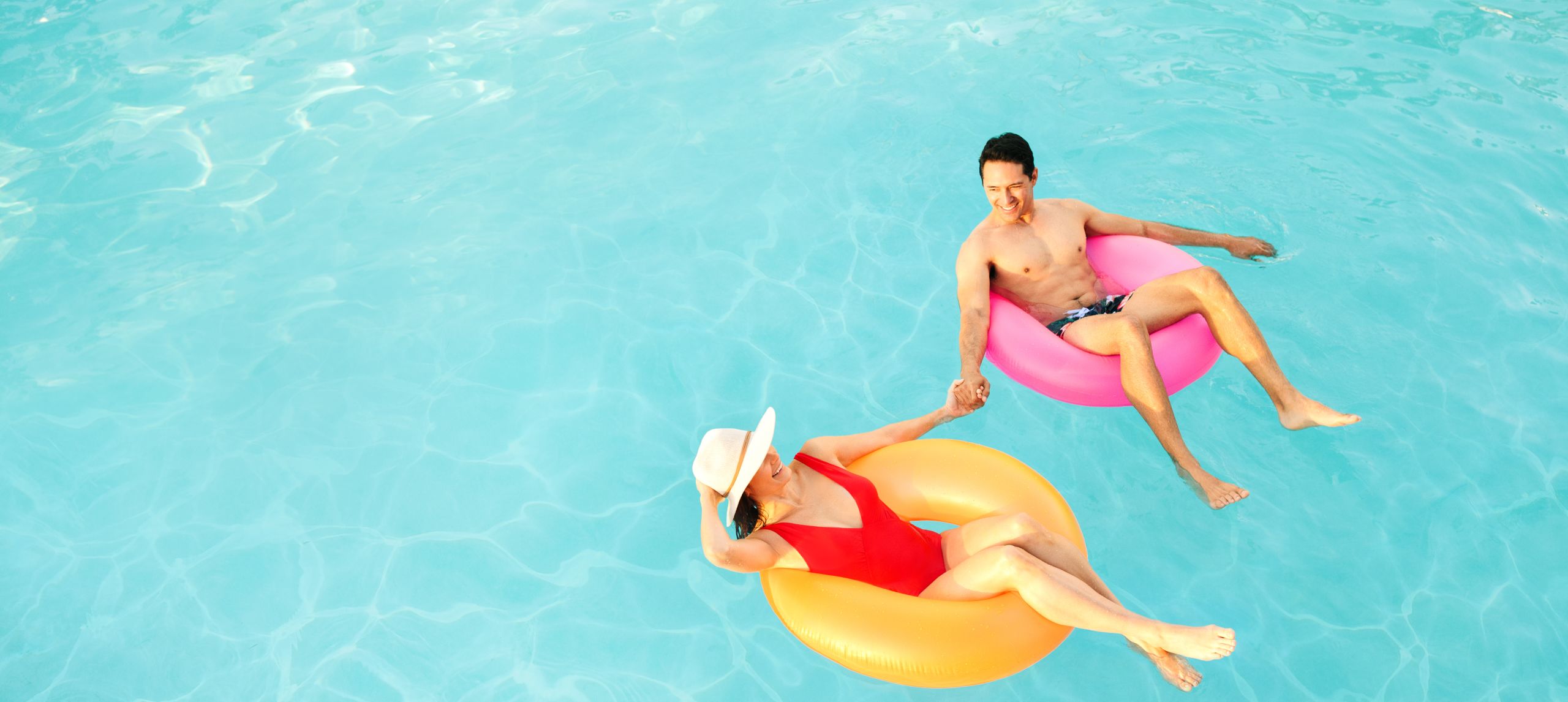 Man and woman relaxing in pool, on rubber rings