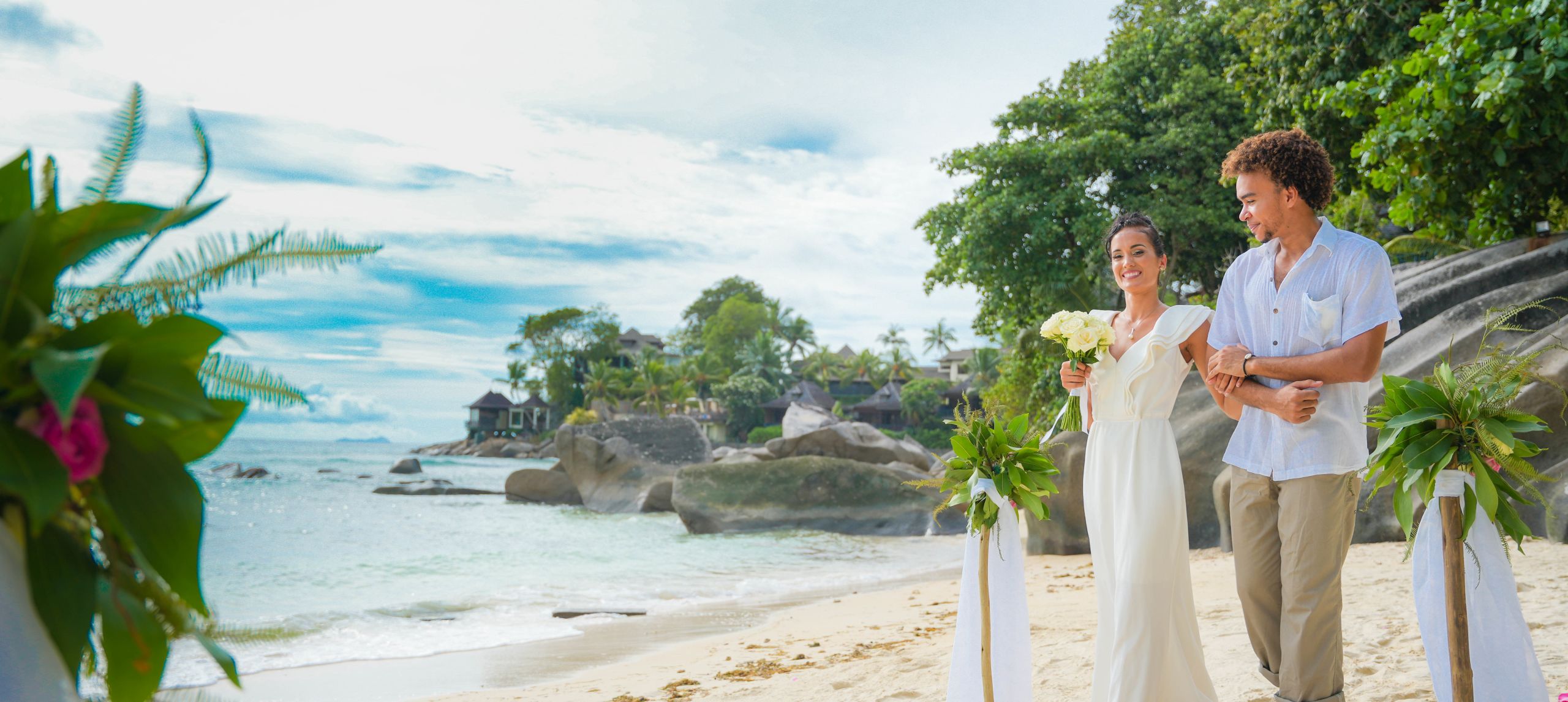 A bride and groom walk down the flower lined isle on the beach.