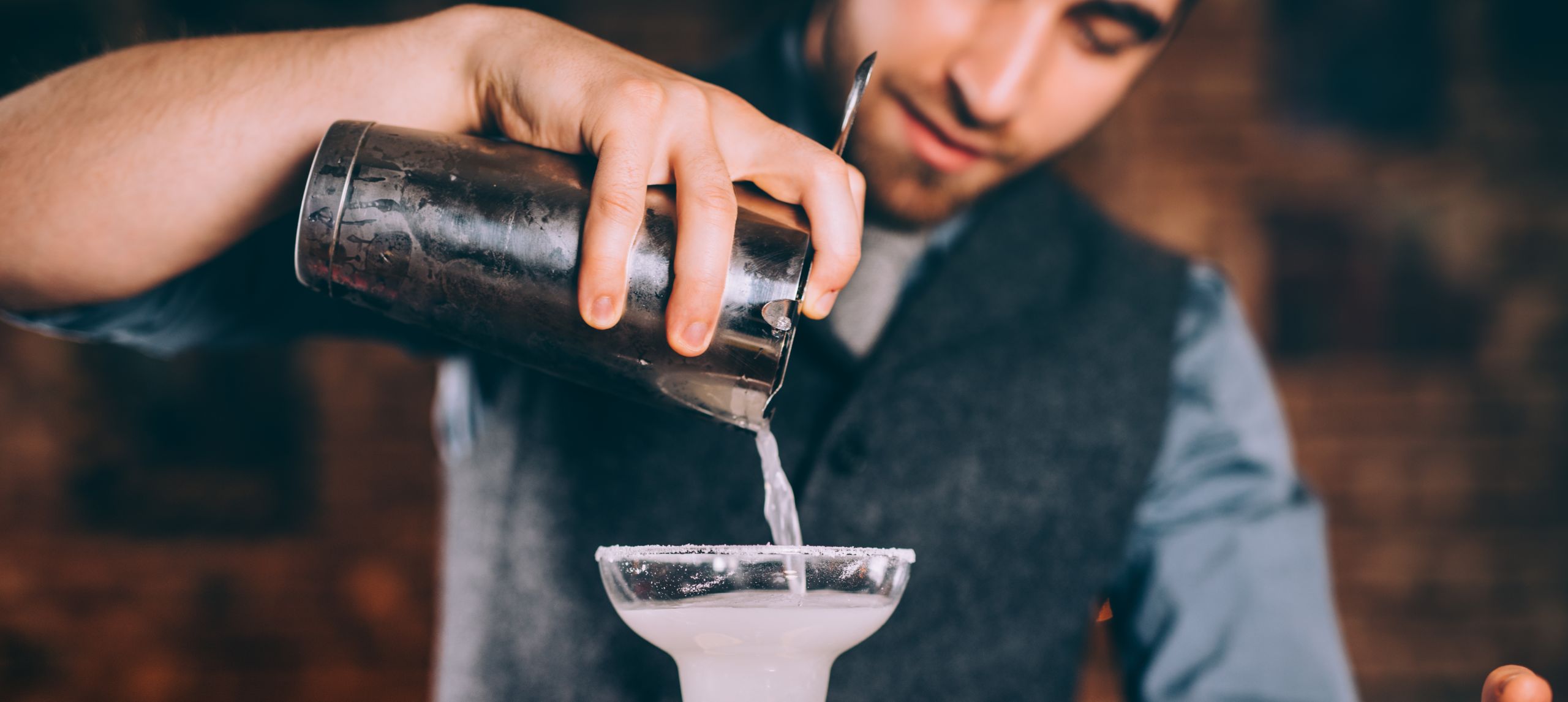 Barman profesional que sirve un cóctel margarita con colador y utensilios para cócteles