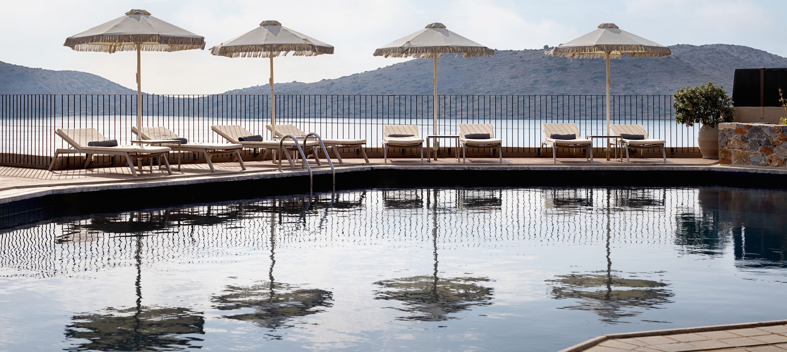 Outdoor pool with sun loungers, parasols, and view of mountains.