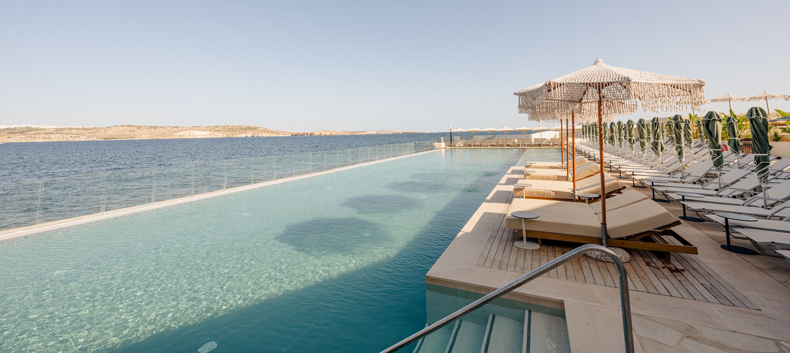 Patio-alue, josta lepotuolit, näkymä uima-altaalle ja merelle aurinkoisena päivänä