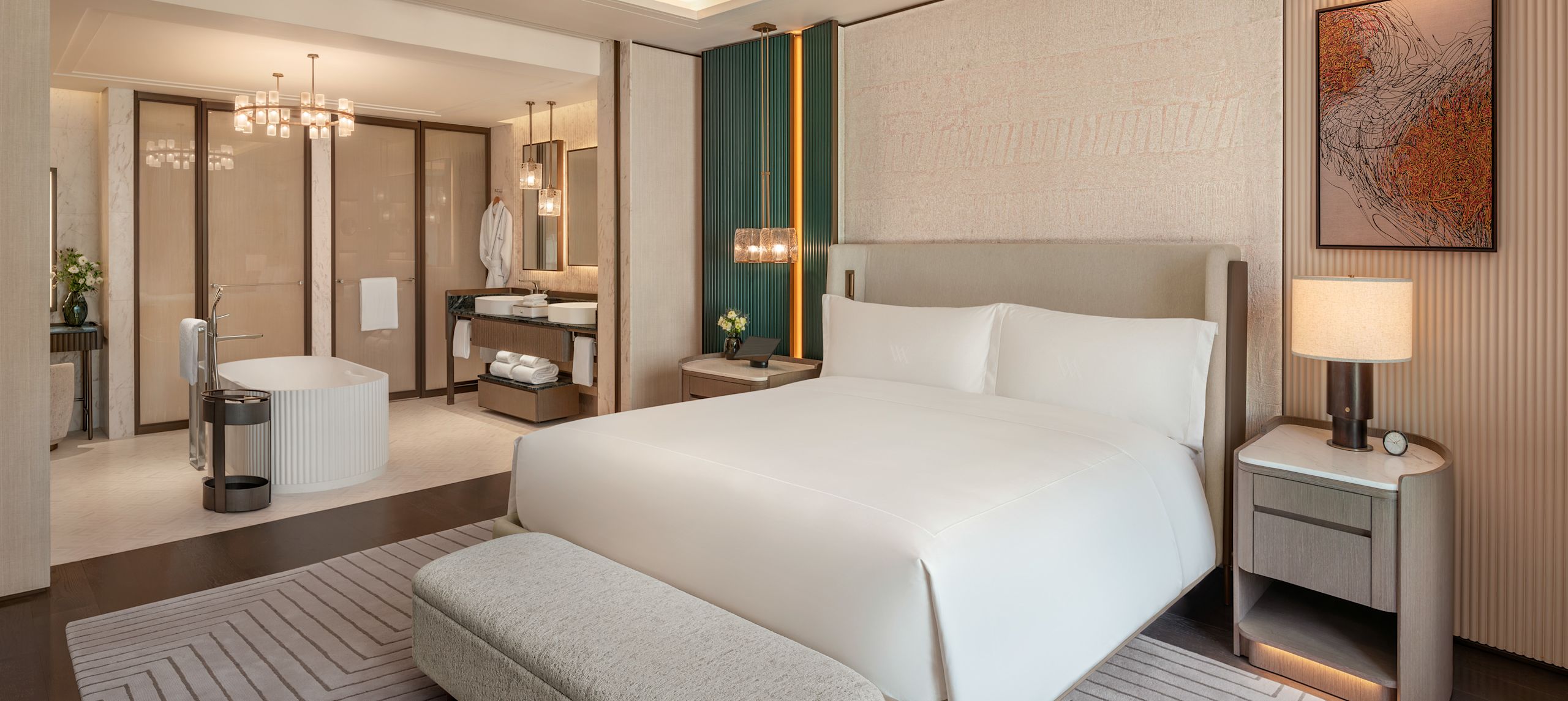 Quarto da suíte com cama king-size, banco estofado, cadeira confortável e transição para o banheiro