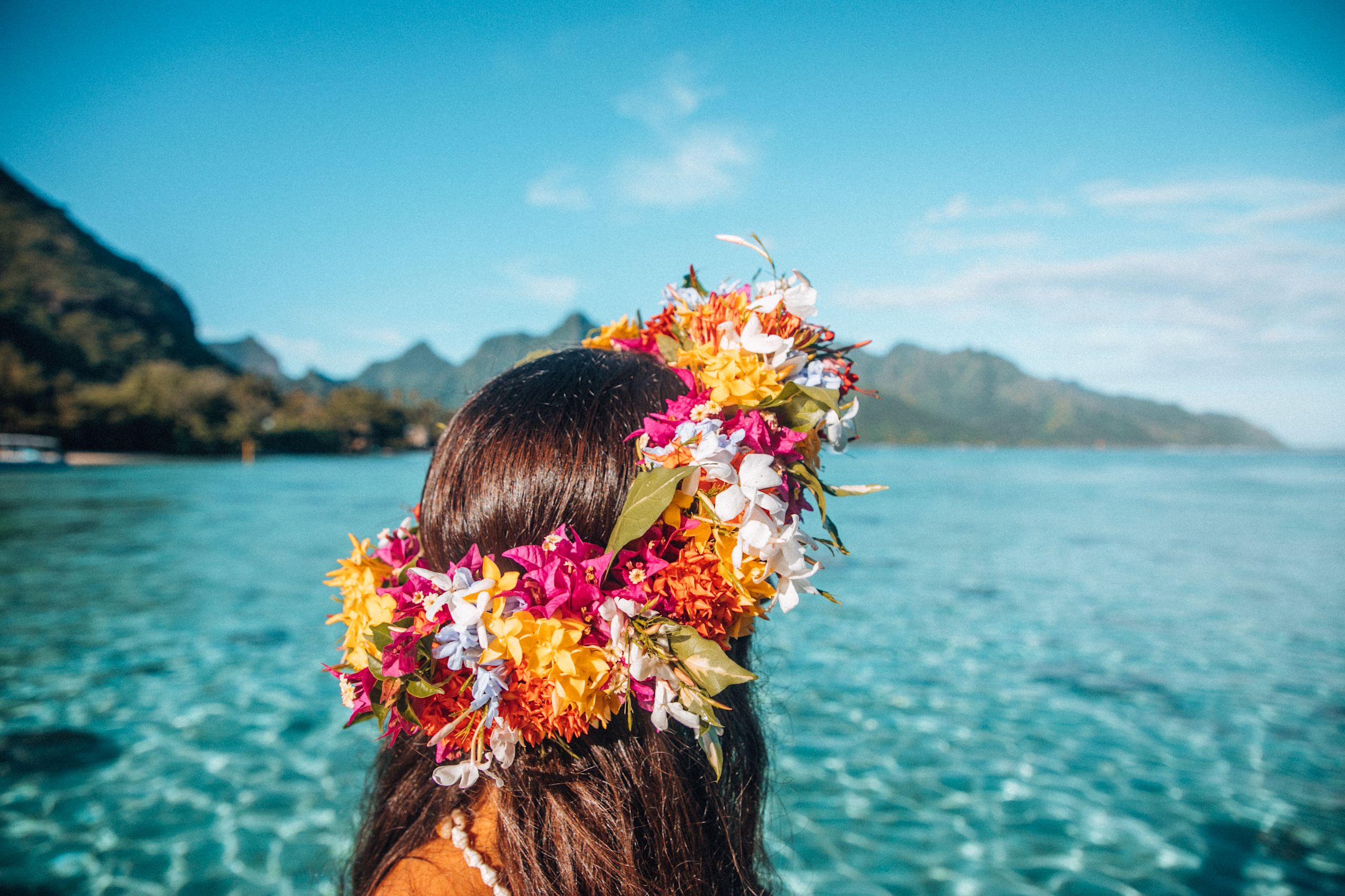 Female gazing out to the blue ocean wearing brightly colored flower crown