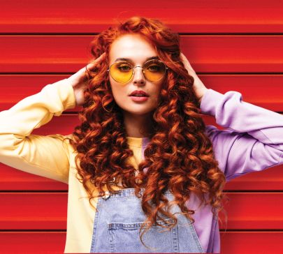 Woman with red hair and orange sunglasses in front of red slats