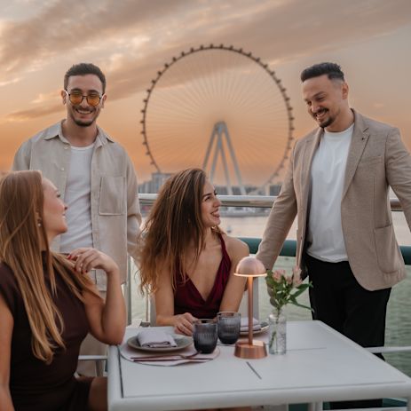 Două cupluri luând masa pe o terasă a restaurantelor la apus