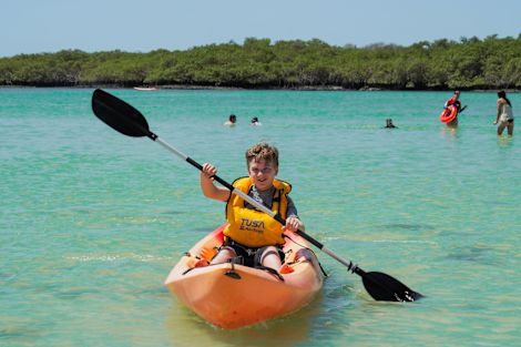 People Swimming and a Boy Padding a Canoe on the Water