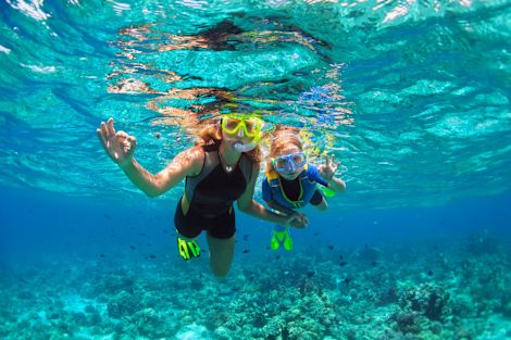 Mother and kid in snorkeling mask dive underwater with tropical fishes in coral reef sea pool. Show by hands divers sign O