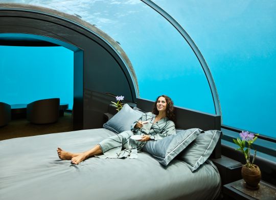 Woman relaxing on bed in underwater guest room. Fish can be seen through the glass ceiling