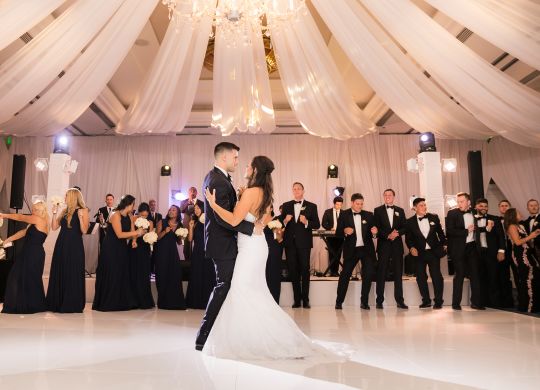 Bride and groom dancing on ballroom floor surrounded by guests