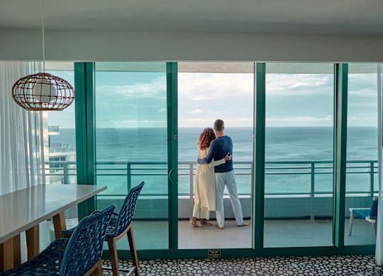 Bărbat și femeie îmbrățișându-se în timp ce stau la balconul exterior cu vedere spre ocean