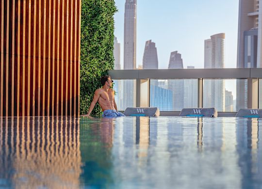 Man relaxing at edge of pool with city view