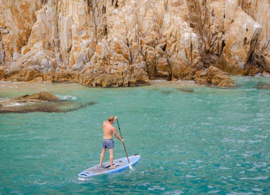 Hombre remando en el mar, con acantilados detrás
