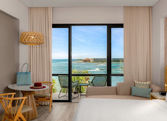 Grand lit, canapé, table et balcon dans une chambre avec vue sur l'océan