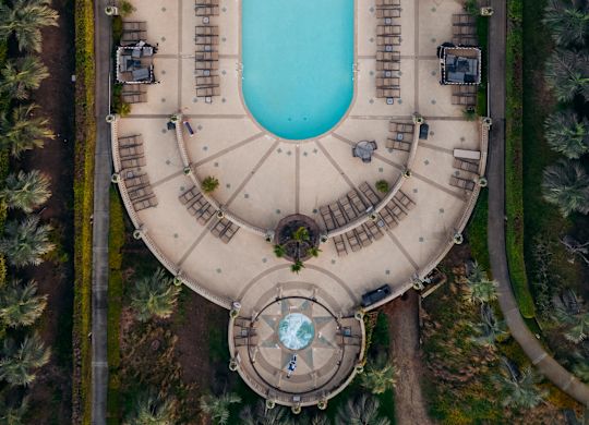 Widok z lotu ptaka na basen zewnętrzny ze strefą wypoczynkową i drzewami palmowymi