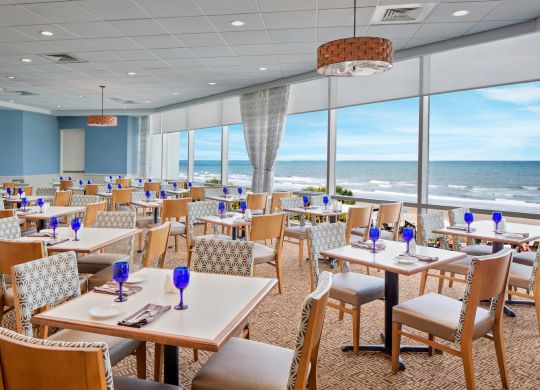 Stoly a židle v kavárně Cafe Amalfi s velkým oknem s výhledem na oceán