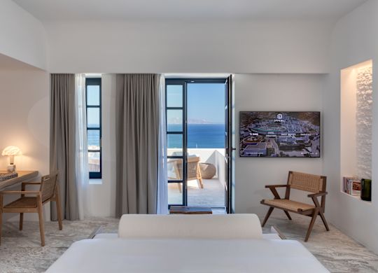 Queensize-Bett im Zimmer mit weißer Bettwäsche und Balkon mit Meerblick. 