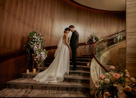 Wedding Couple Standing at Ballroom Stairs with Flowers
