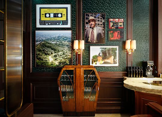 Side Hustle bar with dark green walls, a wooden wine cabinet, framed vintage photos and a yellow cassette tape on the wall.