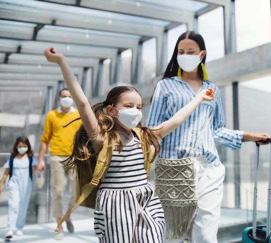 Familie mit zwei Kindern, die im Urlaub sind und Gesichtsmasken am Flughafen tragen.