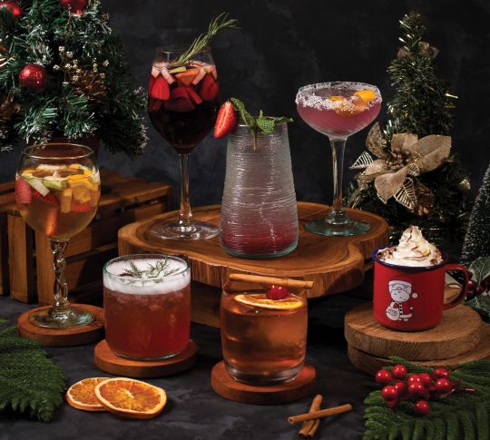 A variety of cocktails sitting on natural wood slices with small decorated Christmas trees throughout.