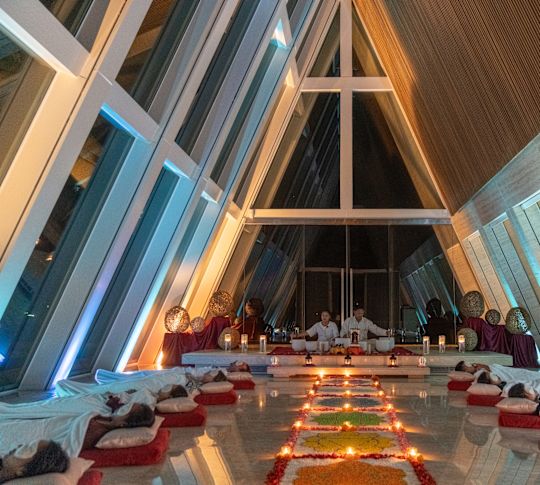 Tiga orang berpartisipasi dalam penyembuhan dengan suara kristal di kamar dengan jendela setinggi langit-langit dan beragam lilin.