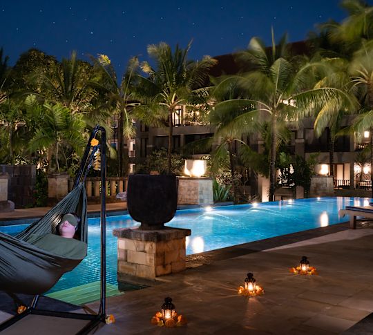 Wanita berbaring di tempat tidur gantung di bawah bintang, di tepi kolam renang.