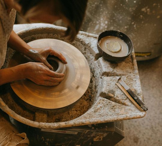 A man's hands turning clay on a pottery spinning wheel at a ceramics workshop.
