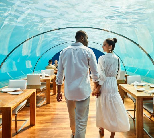 Man and woman walking into underwater restaurant. The ocean can be seen through the glass ceiling