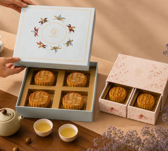 Una donna sta aprendo una scatola con torte di luna su un tavolo con tazze da tè