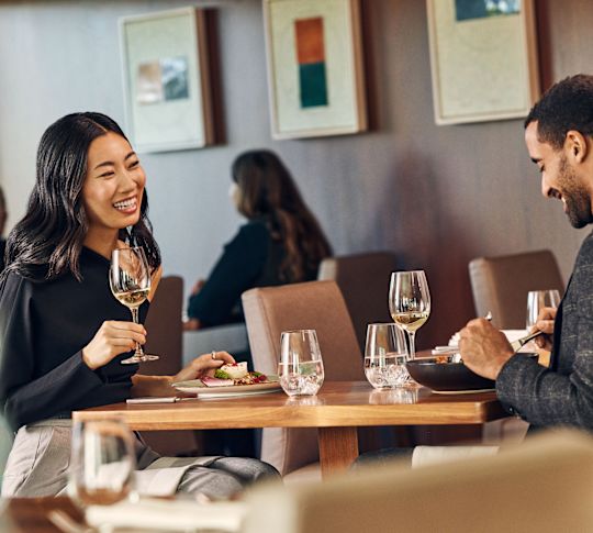 Man and woman smiling as they sit in restaurant area with food and drinks