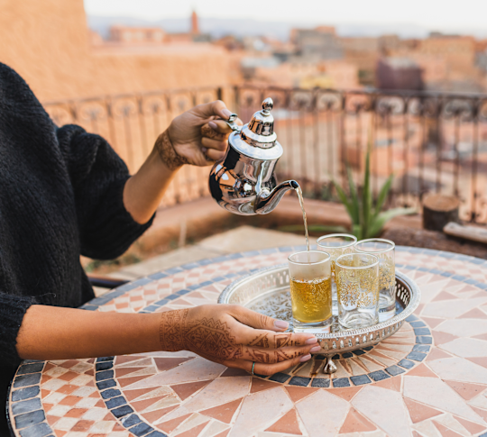 Une personne versant du thé sur une tasse dans une terrasse avec vue sur la ville