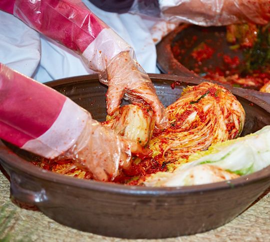 김치를 섞을 때 요리용 장갑을 낀 여성용 손.