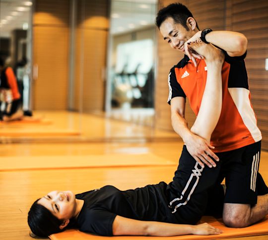 Fitnesstrainer, der einem Gast beim Dehnen hilft