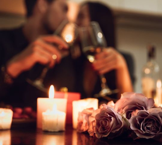 Closup of flowers and candles with couple drinking wine in the background