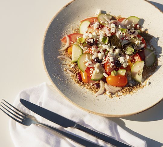 Řecký salát na bílém talíři s okurkou, rajčaty, cibulí, olivami a sýrem feta.