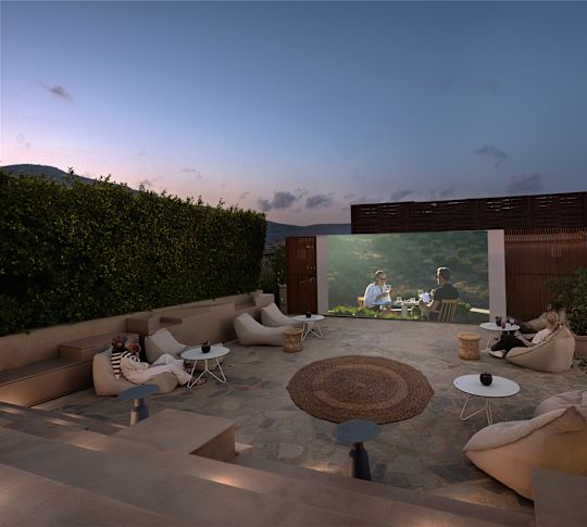 Venkovní posezení v restauraci Amphiteatro s taškami na fazole, malými stoly a velkou obrazovkou zobrazující film.