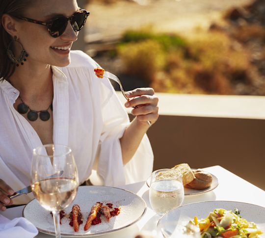 Lidé večeří u venkovního stolu s talíři z grilovaných mořských plodů a sklenicemi vína.