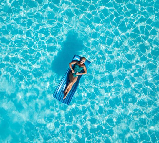 Imagine aeriană a piscinei cu o persoană care plutește pe o suprafață gonflabilă