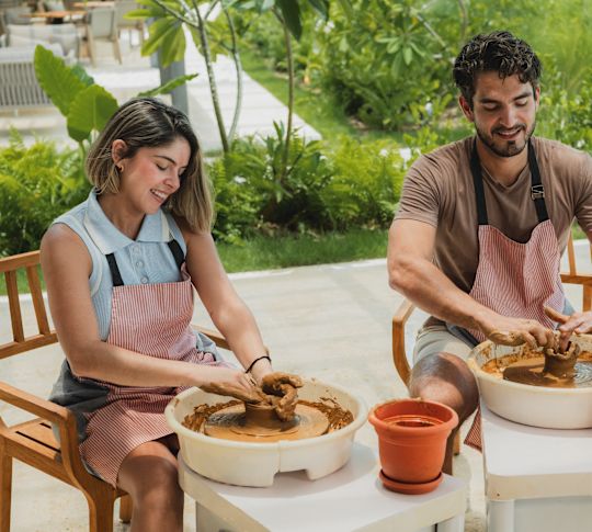 Un cuplu care modelează argila pe roata oliță în timpul unei clase de olărit.