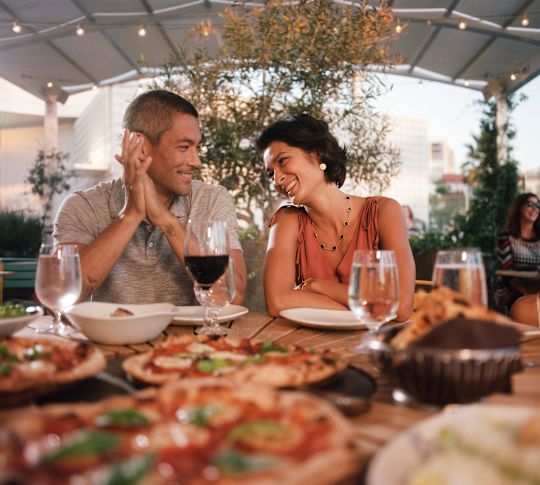 Paar sitzt am Esstisch in einem Pavillon mit Pizza