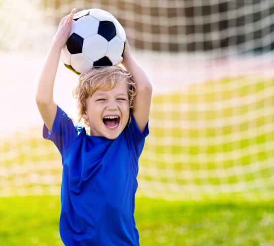 Boy Holding a  Soccer Ball in a Field with a Goal Net