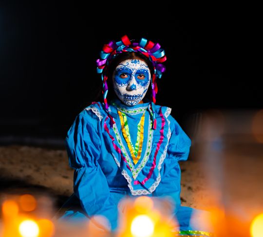 A Woman Dressed in a Costume is Sitting in an Area with Lit Candles to Celebrate el Dia de los Muertos