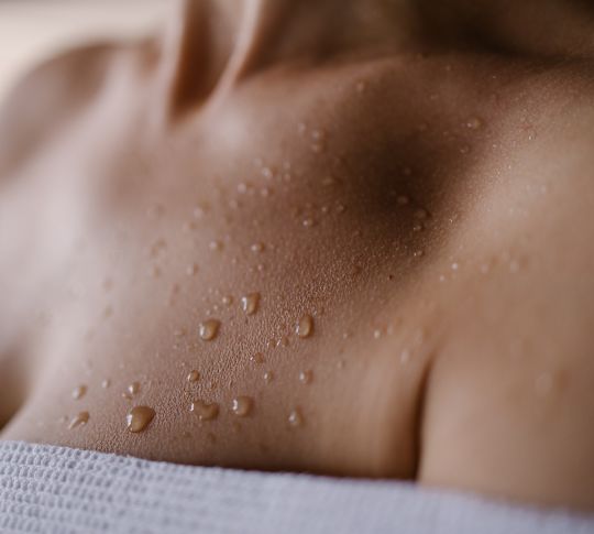 Contas de água passam pela parte superior do tórax de uma mulher usando roupão branco