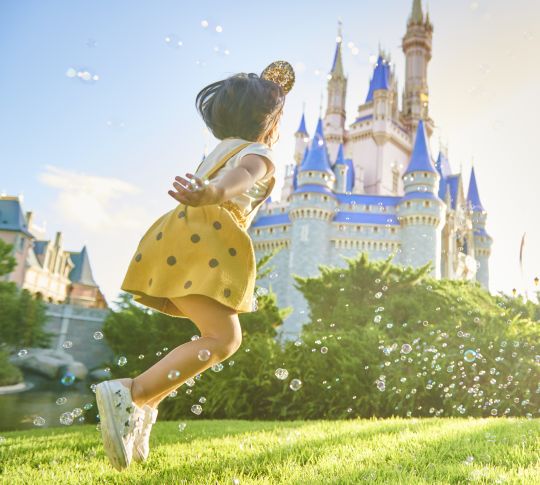 Girl on a garden playing with bubbles and looking at Disney Castle