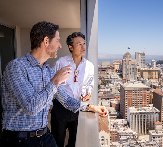 Two men enjoying the city view from their guest room balcony